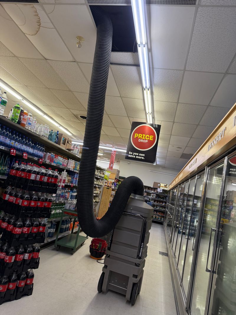 A wheeled vacuum in a grocery aisle, its hose running up into the ceiling
