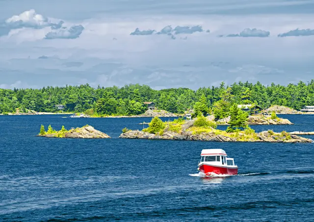 Boat passing rocky, pine-covered islands on a lake