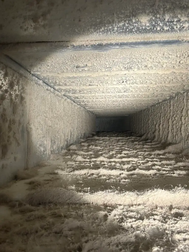 A close-up view inside a dirty air duct covered with thick dust and debris, highlighting the importance of duct cleaning Muskoka or Huntsville Ontario homeowners need to maintain clean, healthy air.