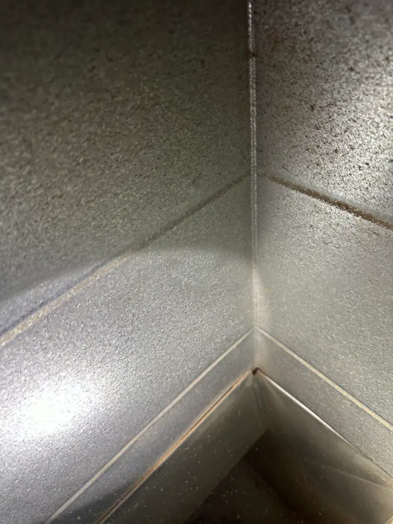 A close-up view of the corner of a metallic surface, possibly a stainless steel sink or industrial container, with visible seams and some spots of grime—reminding us how duct cleaning can help maintain indoor air quality in such environments.