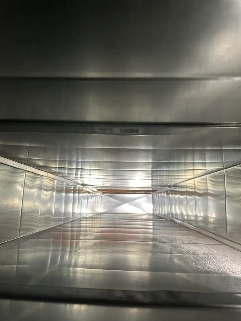 View looking down the inside of a metal air duct, showing shiny, reflective silver walls and a rectangular tunnel that narrows into the distance with light visible at the far end—ideal results after professional duct cleaning Muskoka.