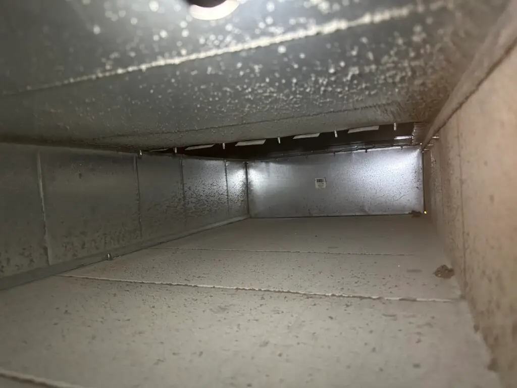 The image shows the inside of a metal air duct, with dusty surfaces and dirt build-up along the bottom and sides—clear signs that professional duct cleaning may be needed to improve air quality.