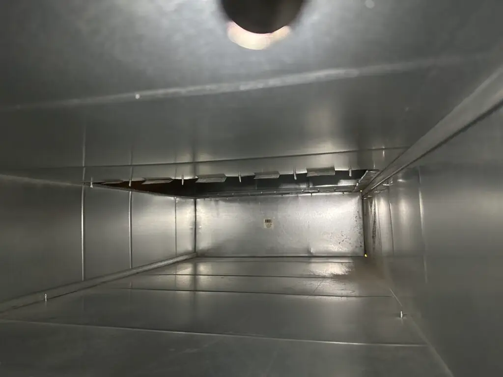 View inside a clean, empty air duct with reflective metal walls and a small vent visible at the far end, illuminated by overhead light—an example of how professional duct cleaning Muskoka services can enhance indoor air quality.